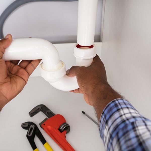 Close-up Of Plumber Fitting Sink Pipe In Kitchen At Home